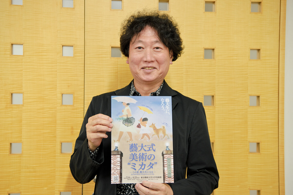 展覧会のチラシを手に微笑む古田先生